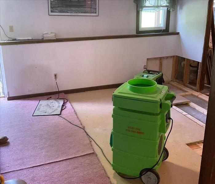 SERVPRO equipment in a water-damaged room with damaged flooring, pulled-up carpet, and visible home framing from demolition