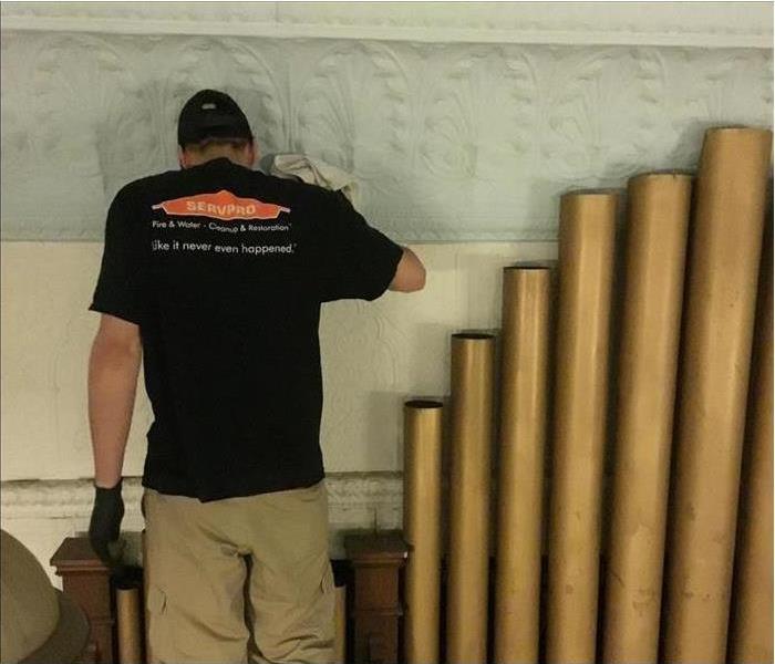 SERVPRO tech cleaning dirt from a wall beside a pipe organ