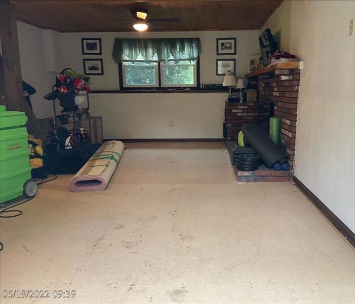 A bare living room floor with some SERVPRO equipment, home contents, a fireplace and rolled-up carpet and pad