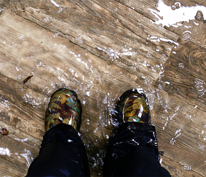 a person in boots standing in a flooded room with hardwood floor